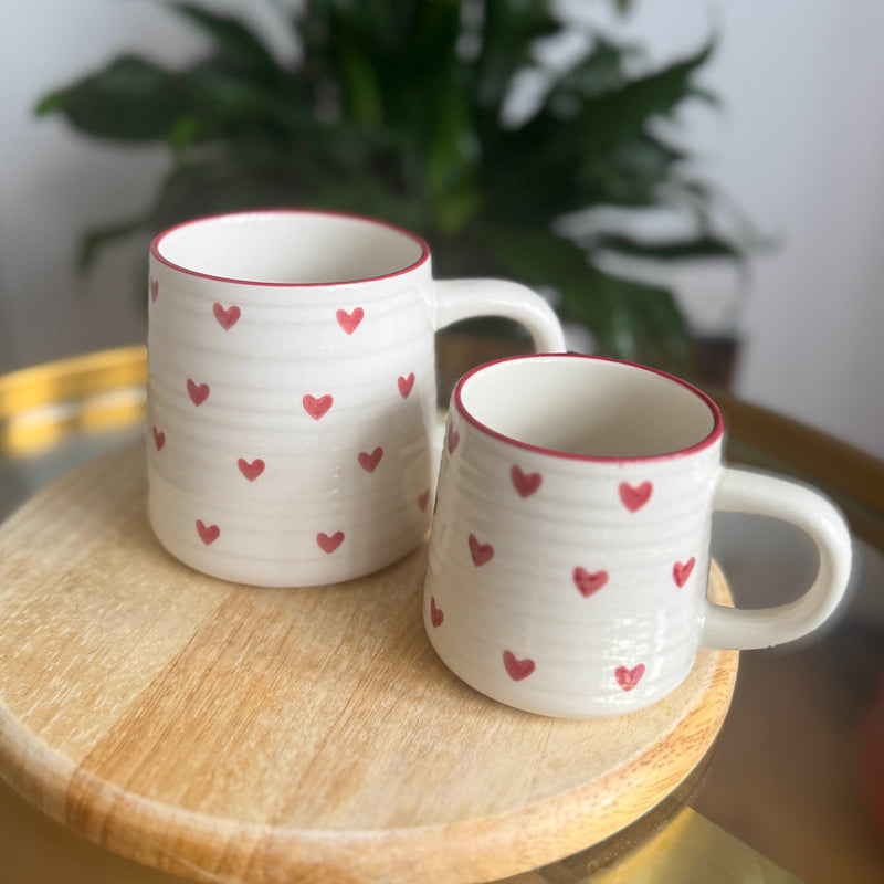 Two ceramic mugs with red heart patterns on a wooden table.